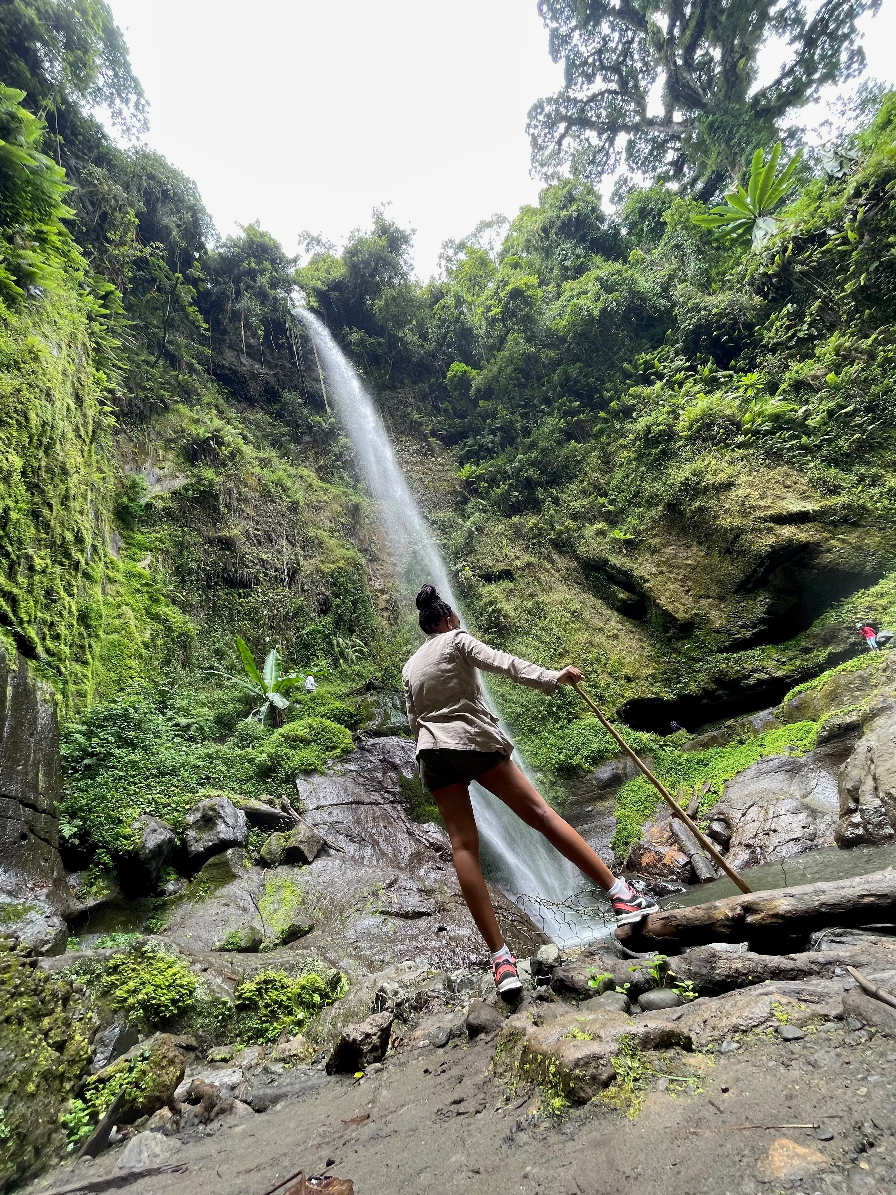 Violet standing in front of Napuru Waterfalls with a walking stick